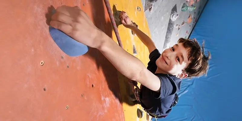 Smiling boy on an indoor rock wall, gripping the next climbing hold