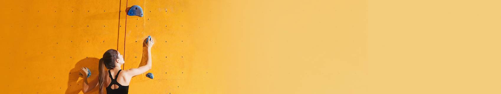 Woman climbing a yellow indoor rock wall, reaching for the next hold